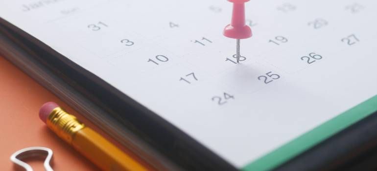 Red pushpin marking a date on a wall calendar beside a pencil and ruler