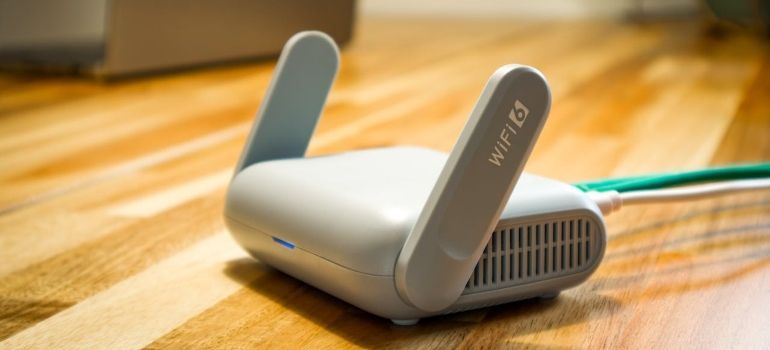 White Wi‑Fi router with two antennas on a wooden desk, with a green Ethernet cable connected