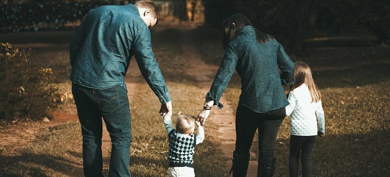 Two adults and two children walking hand in hand through a wooded path at dusk