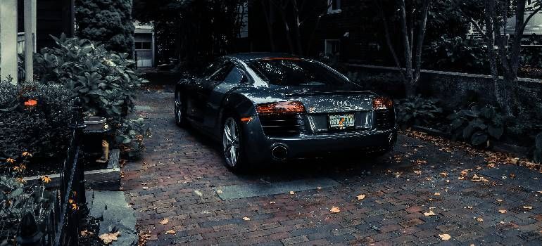 Black luxury car parked on a leaf-strewn driveway in a dark, wooded setting