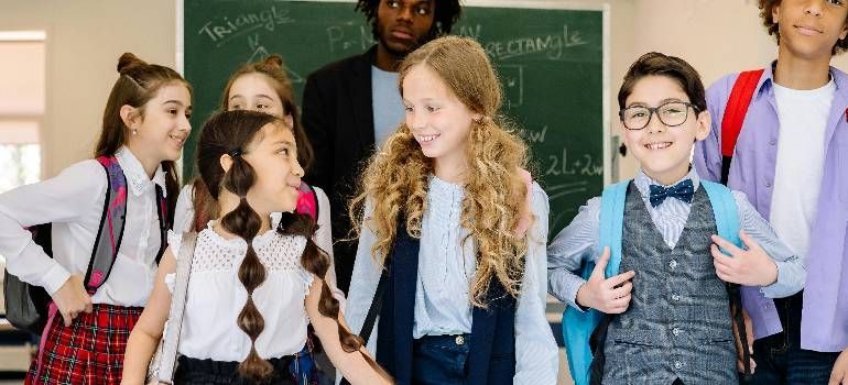 Students standing in a classroom, smiling and talking in front of a chalkboard