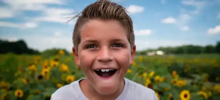 Smiling boy in a white shirt in a sunflower field under a blue sky