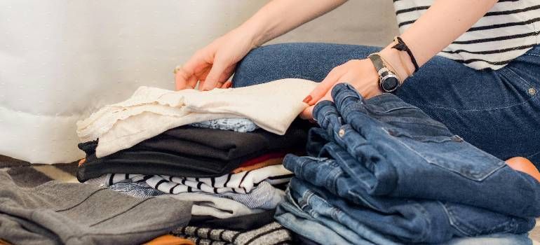 Person folding a stack of clothes on a bed or couch