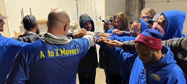 AtoZ Movers team in blue shirts stacking hands in a moving truck, cheering together