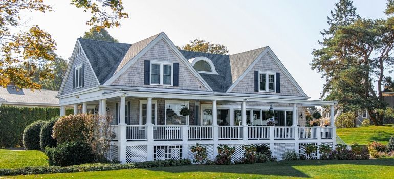 White farmhouse with wraparound porch and manicured lawn under a clear sky