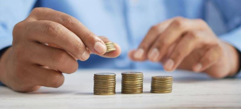 Hands placing coins beside stacked coins on a table, symbolizing saving money