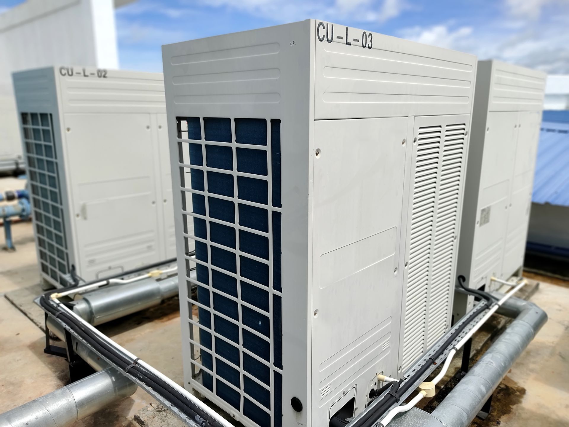 HVAC rooftop units and piping on a building roof, with one white air conditioner in the foreground