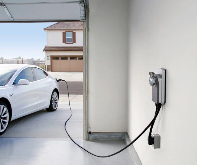 White Tesla charging in a garage, plugged into a charger mounted on the wall.