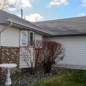 A white-sided home exterior with a brick accent, a bay window, a gravel garden bed, and a white birdbath in the yard.