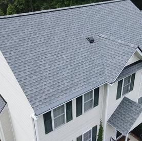 An aerial view of a multi-story house with a grey shingled roof, light siding, and dark window shutters.