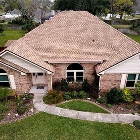 An aerial view of a tan brick suburban house with a brown shingled roof.