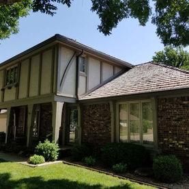 A two-story Tudor-style home with a brick and cream-colored exterior, a shingled roof, and green landscaping.