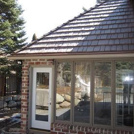 A brick building exterior with a white door, large windows, and a brown shingled roof under a bright sky.