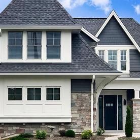 Two-story home with gray shingle roof, white siding, stone accents, dark trim, and a prominent front entrance.