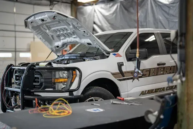 White sheriff's truck with hood open in a garage, tools on table in front.