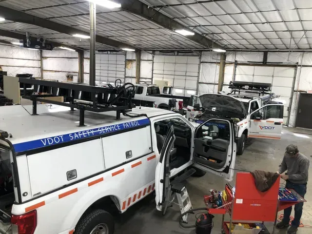 VDOT Safety Service Patrol trucks parked in a garage. A person works on one.