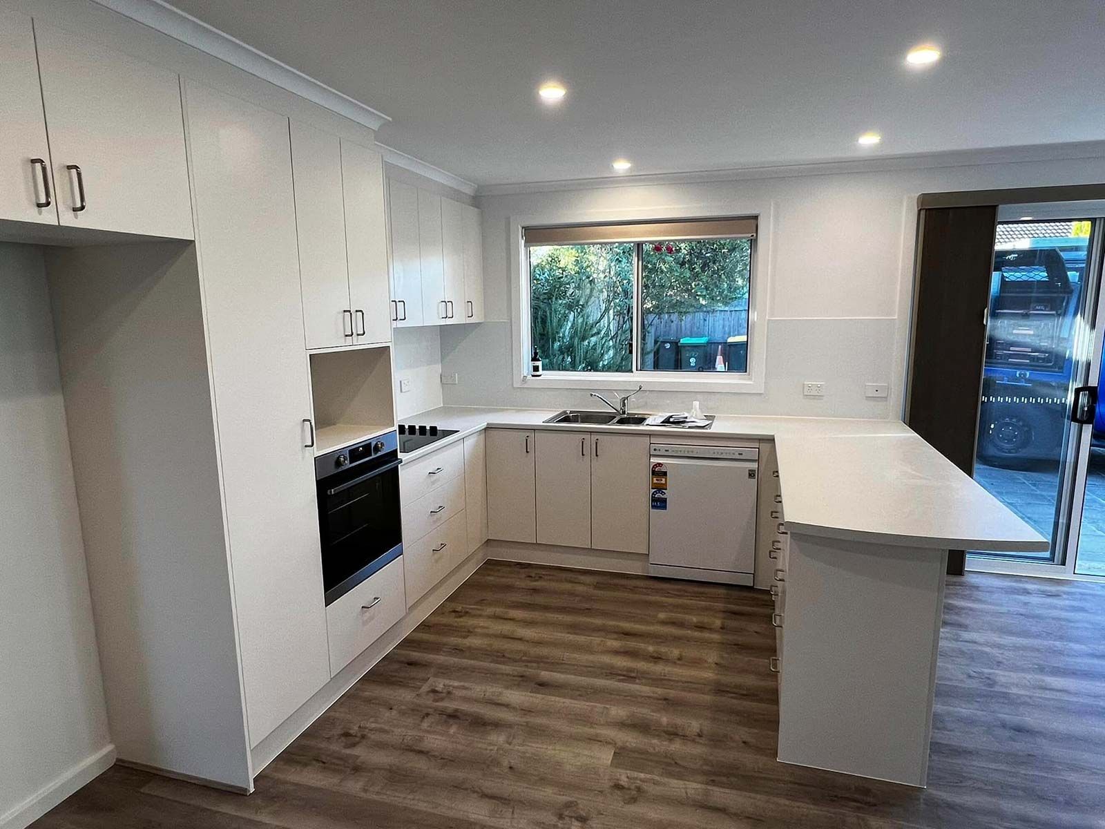 A Kitchen With White Cabinets, A Stove, A Sink, And A Window — P & M Maintenance Building Services in Yass River, NSW