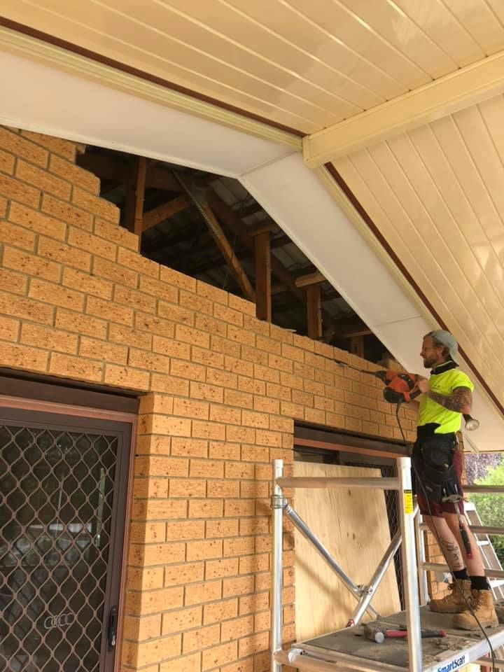 A Man Is Standing on A Scaffolding Working on A Brick Wall — P & M Maintenance Building Services in Yass River, NSW