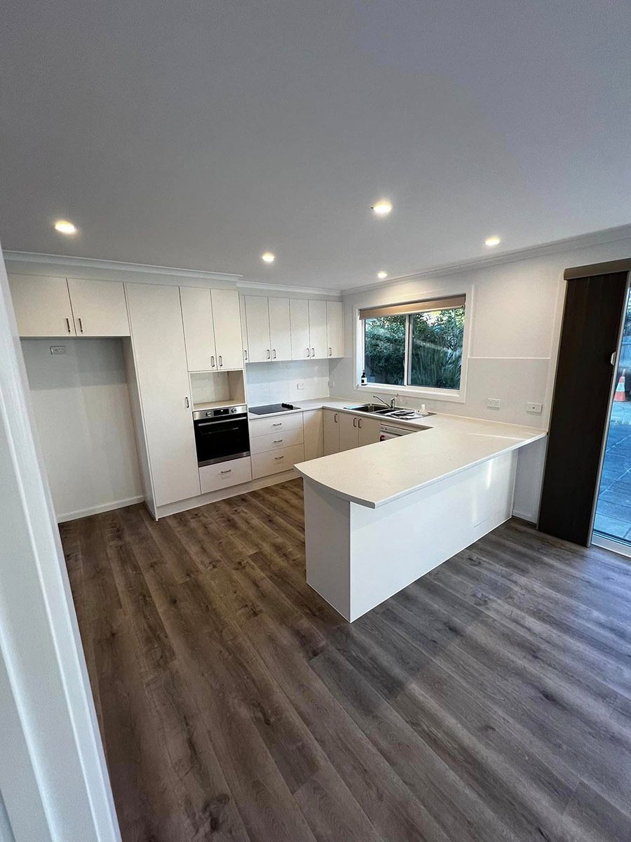 A Kitchen With Hardwood Floors, White Cabinets — P & M Maintenance Building Services in Canberra, ACT