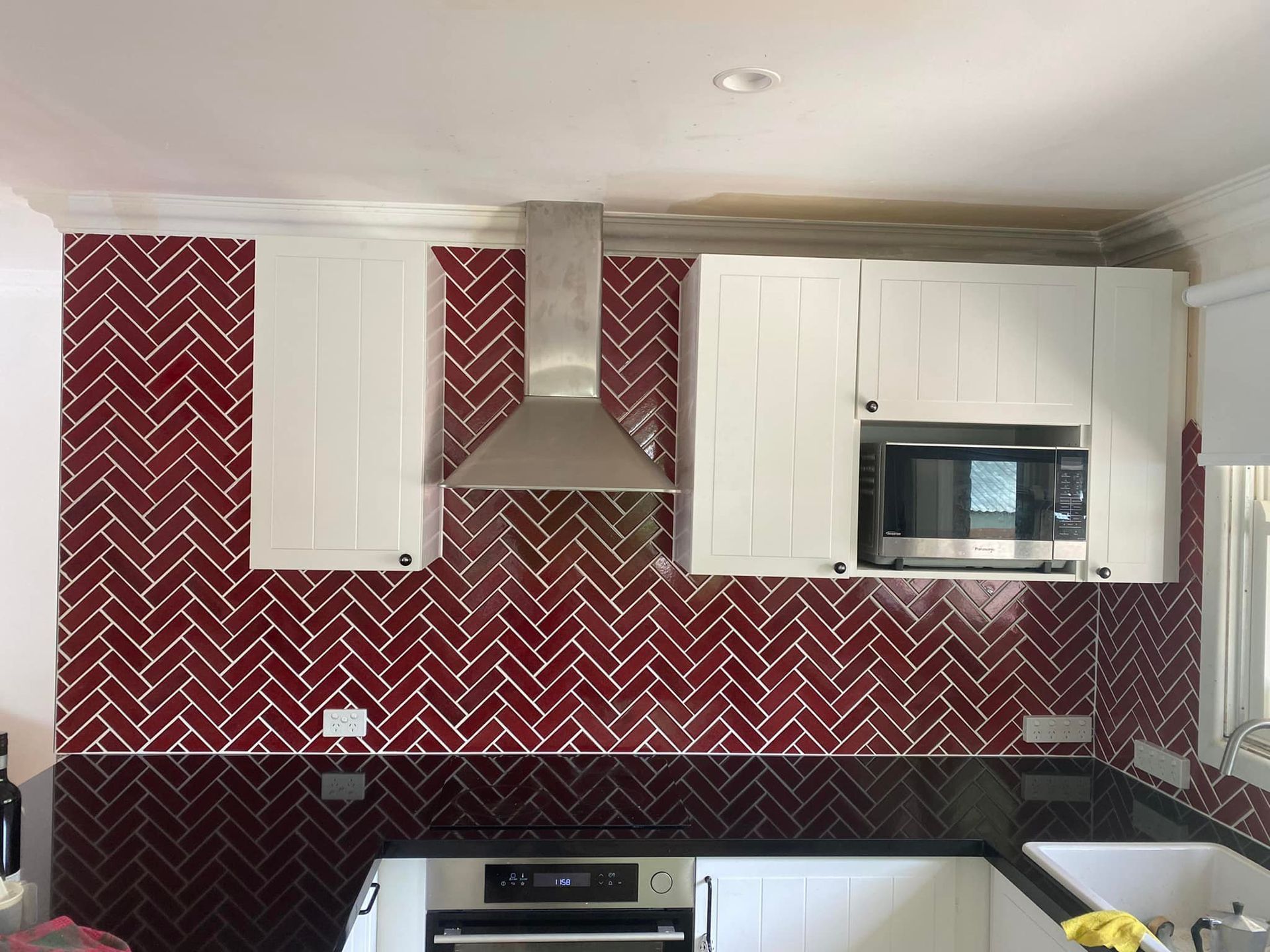 A Kitchen with Red Herringbone Tiles and White Cabinets — P & M Maintenance Building Services in Gungahlin, ACT