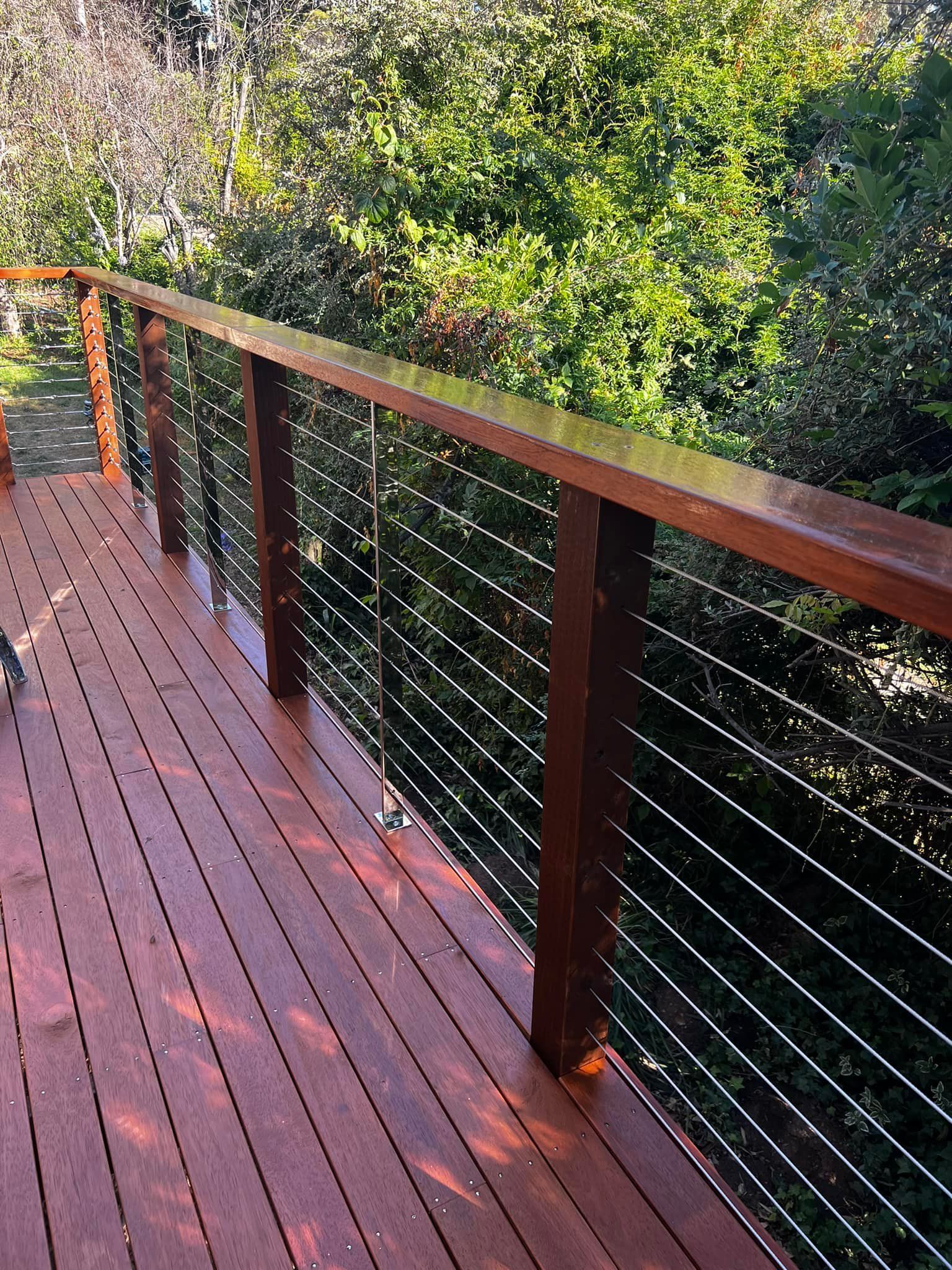 A Wooden Deck with A Metal Railing and Trees in The Background — P & M Maintenance Building Services in Yass River, NSW