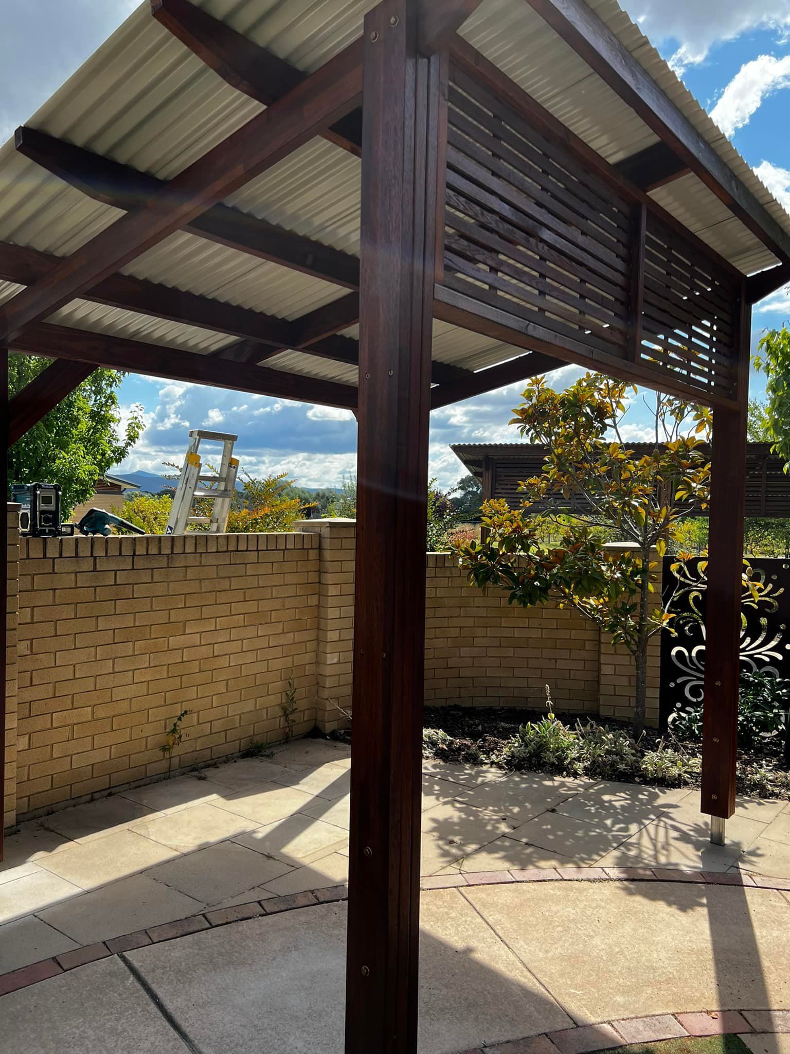 A Wooden Gazebo with A White Roof and A Brick Wall in The Background — P & M Maintenance Building Services in Yass River, NSW