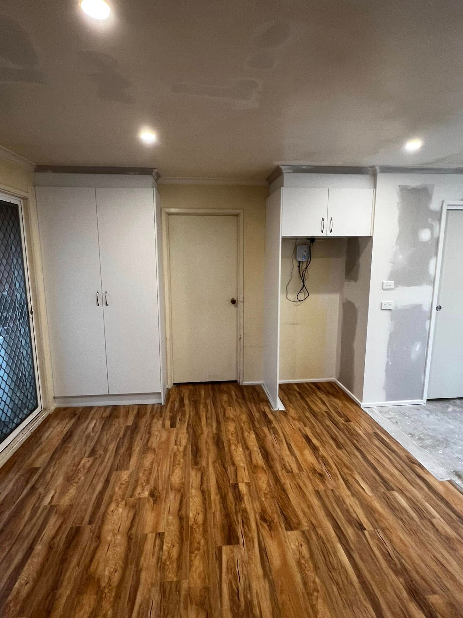 An Empty Room with Hardwood Floors and White Cabinets — P & M Maintenance Building Services in Yass River, NSW