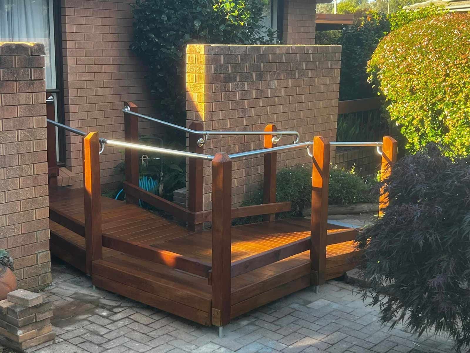 A Wooden Deck With A Brick Wall In The Background — P & M Maintenance Building Services in Canberra, ACT