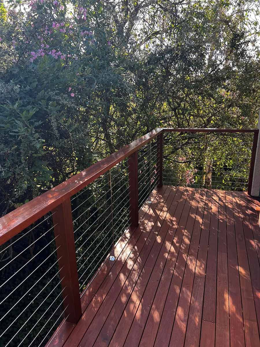 A Wooden Deck With A Metal Railing And Trees In The Background — P & M Maintenance Building Services in Yass, NSW