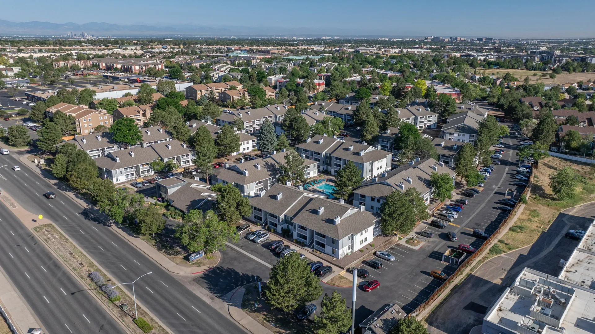 Aerial view of apartment complex with swimming pool, parking lots, and surrounding neighborhood.