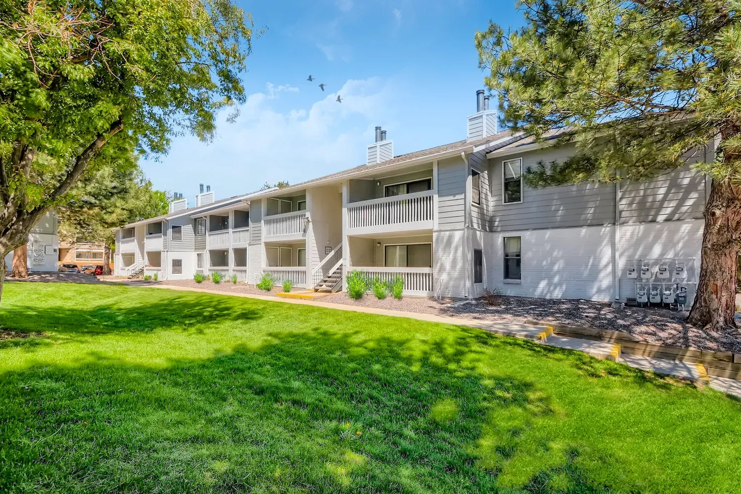 Exterior view of apartment buildings with green lawn and trees.