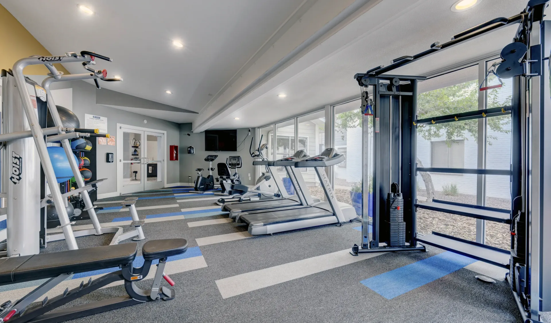 Treadmills and weight machines in a well-equipped fitness center with large windows.