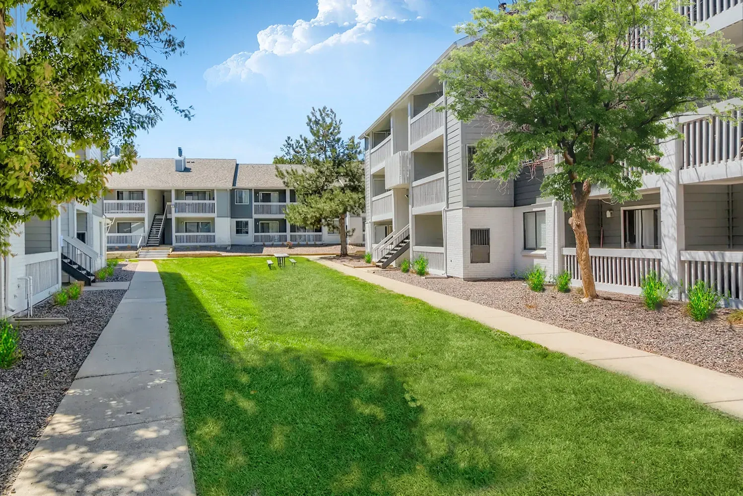 Apartment building exteriors with a grassy courtyard and sidewalk.