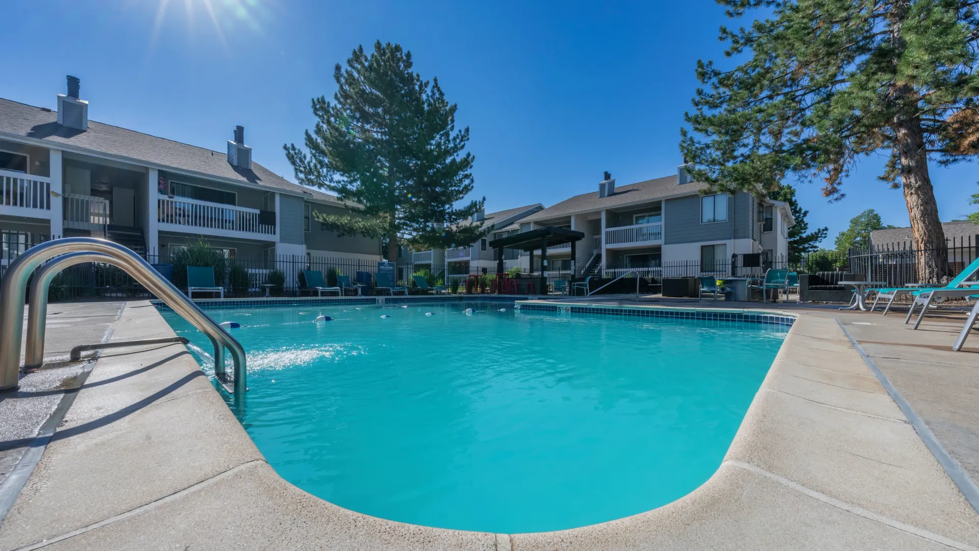Outdoor swimming pool with lounge chairs and apartment buildings in the background.