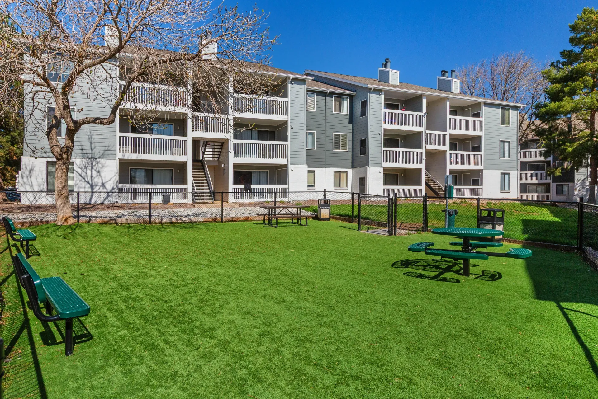 Apartment building exterior with a fenced-in dog park area in the foreground.