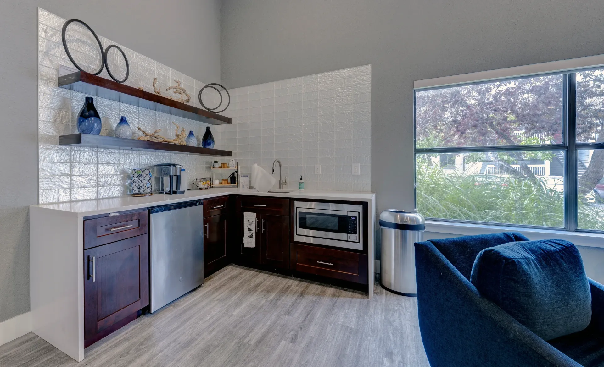 Corner kitchen with dark wood cabinets, stainless steel appliances, microwave, sink, and decorative shelving.
