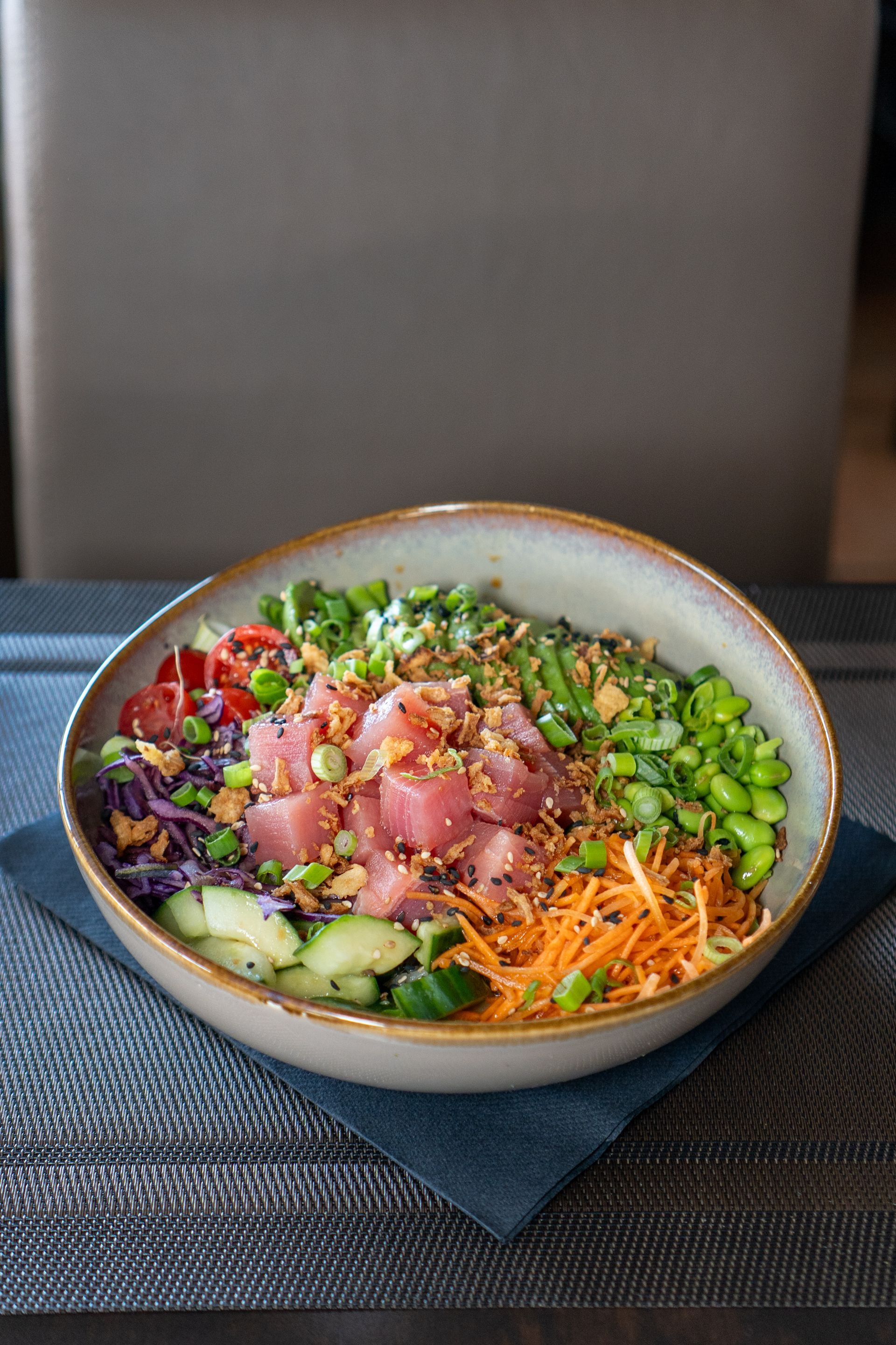 Poke bowl avec thon, légumes et garnitures dans un bol en céramique sur un set de table.