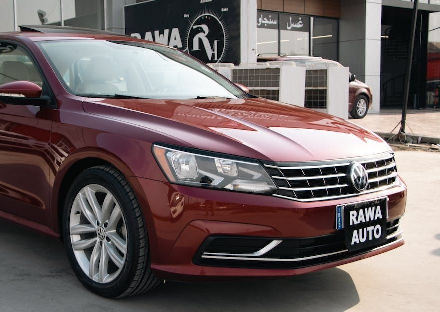 A red volkswagen passat is parked in front of a rowa auto store