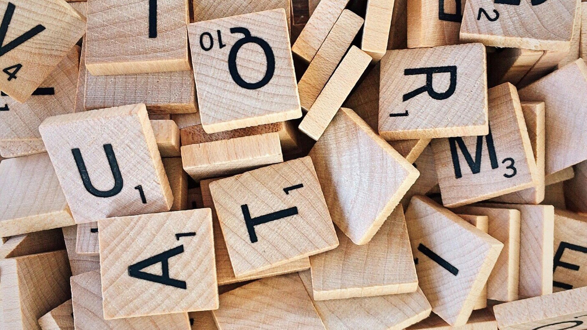 A pile of wooden scrabble tiles with letters and numbers on them.