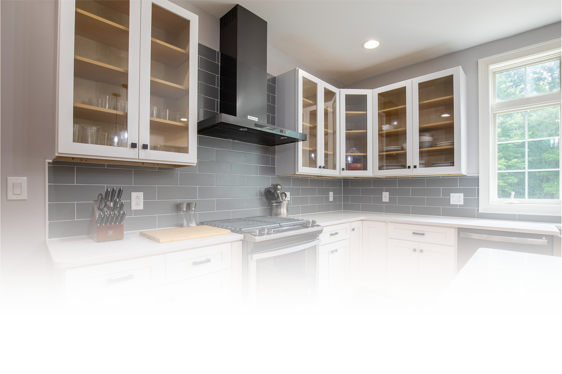 A kitchen with white cabinets , a stove , a dishwasher , and a window.