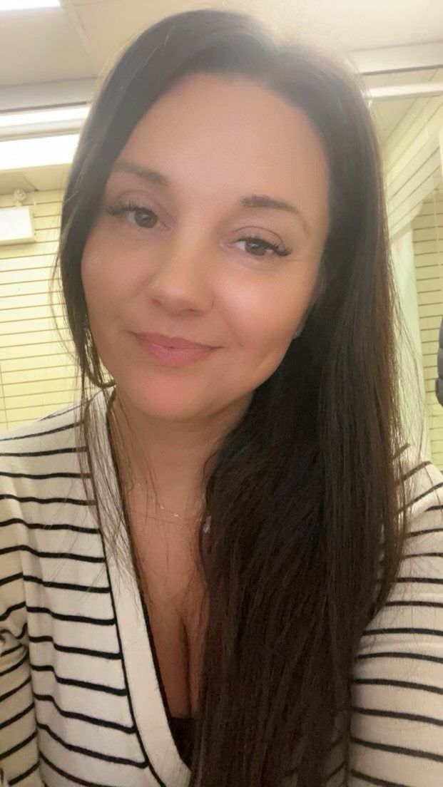 Woman with long brown hair smiles, wearing striped shirt. Indoors.