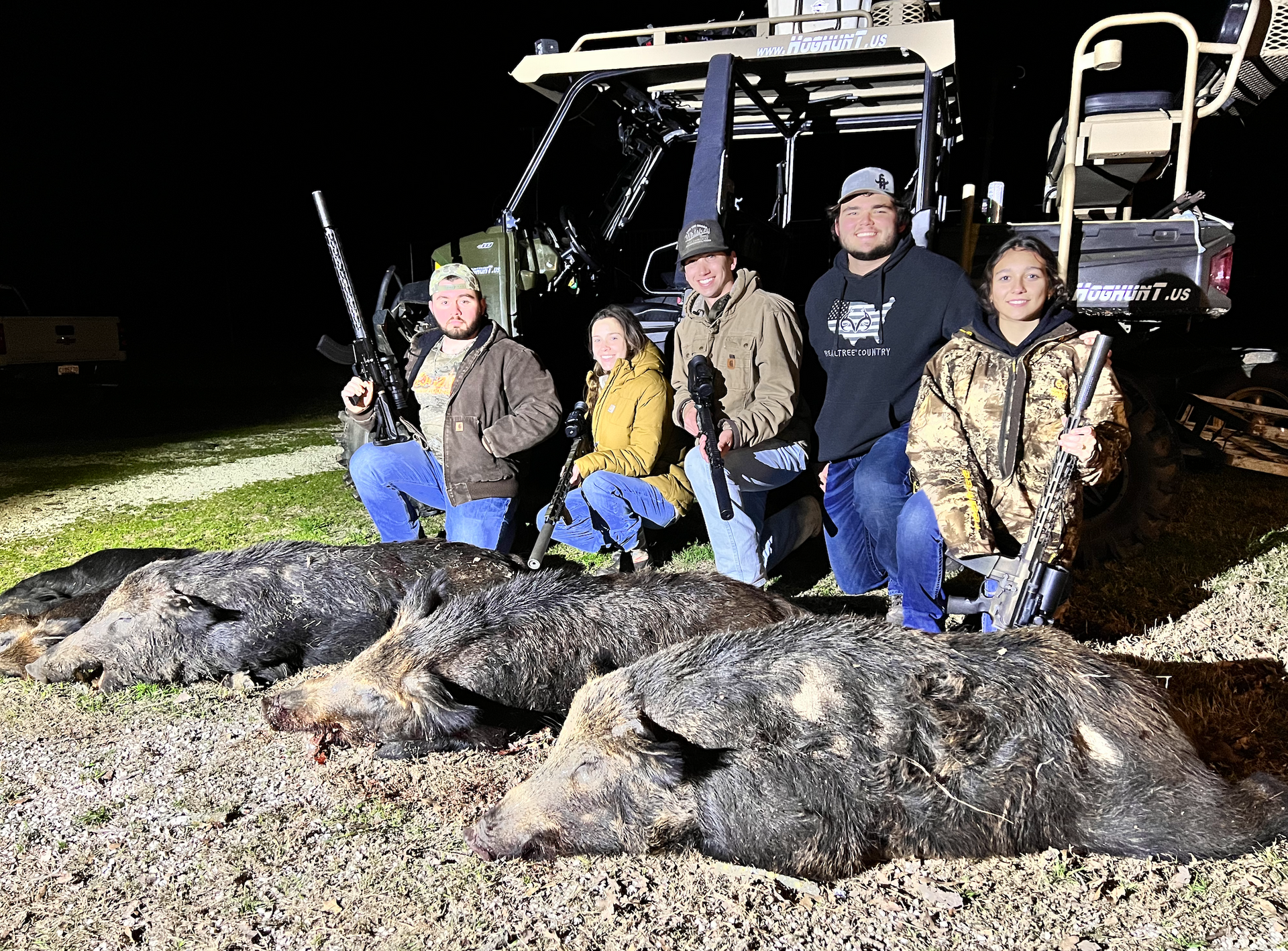 Group of people with rifles pose with harvested wild hogs at night.