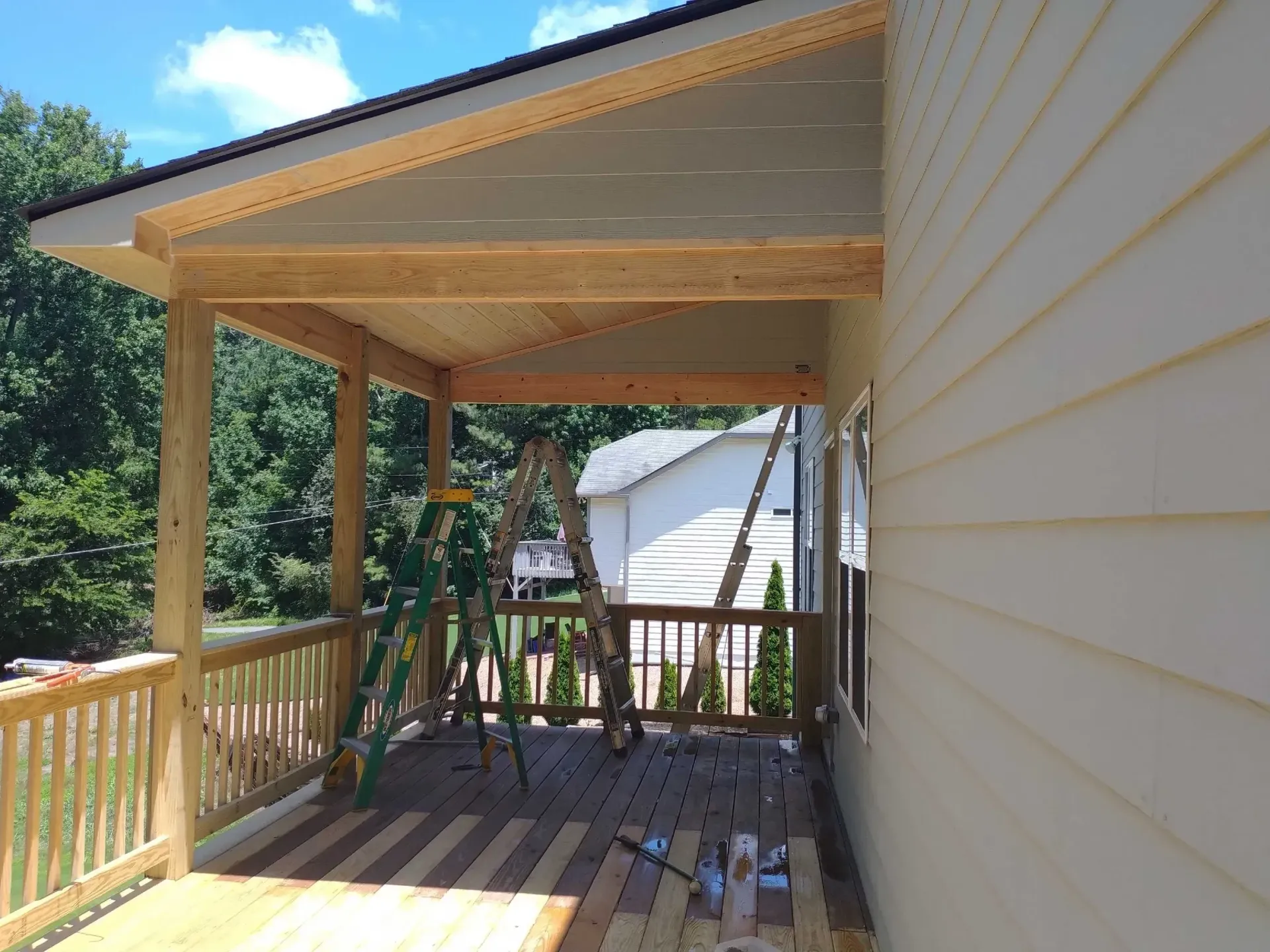 Wooden porch with roof under construction; ladder, railing, and house visible.
