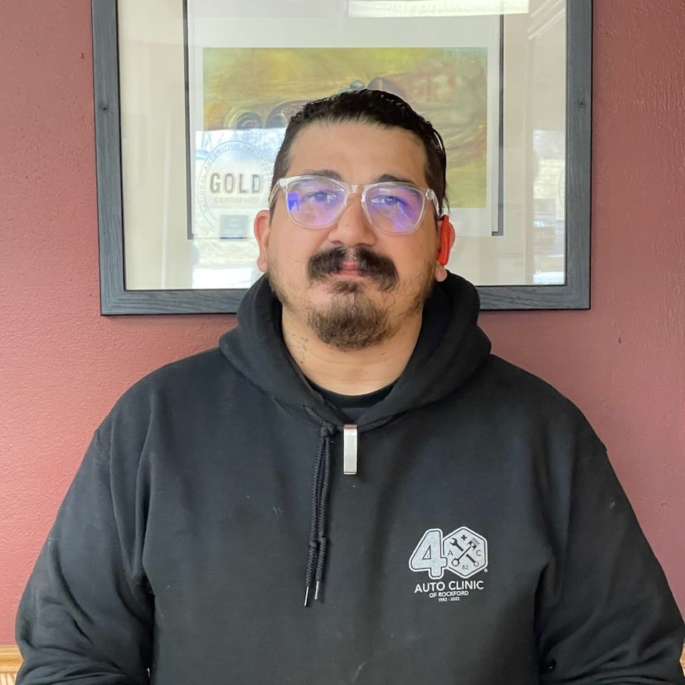 Man in black hoodie and glasses standing indoors against a red wall with framed art behind him