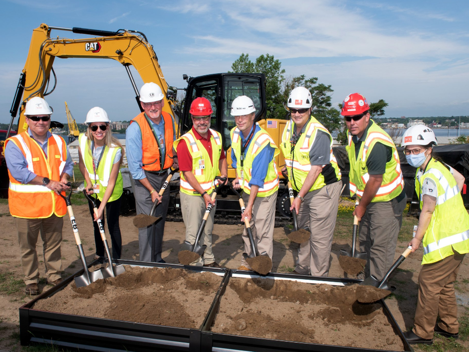 A group of construction workers are shoveling dirt in front of a cat excavator