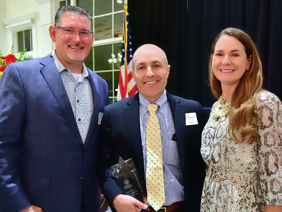 A man in a suit and tie is holding a trophy and posing for a picture with two other people.
