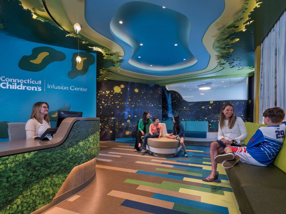 A group of people are sitting in a room with a sign that says connecticut children 's hospital center