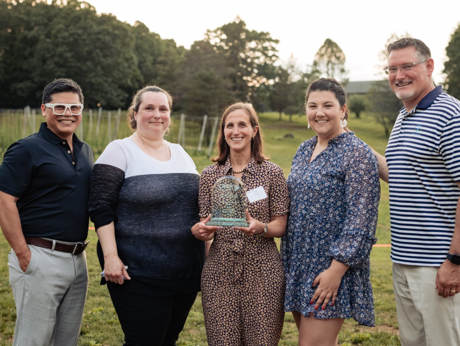 A group of people are standing next to each other in a field holding a trophy.