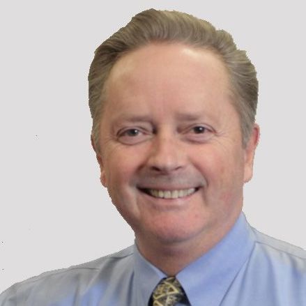 A man in a blue shirt and tie is smiling for the camera.