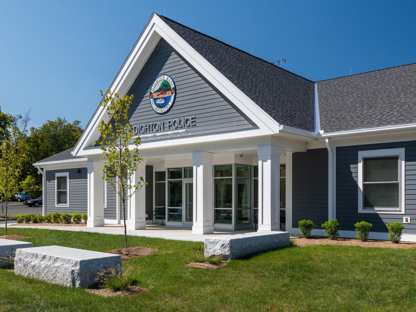A large building with a gray siding and white trim is sitting on top of a lush green field.